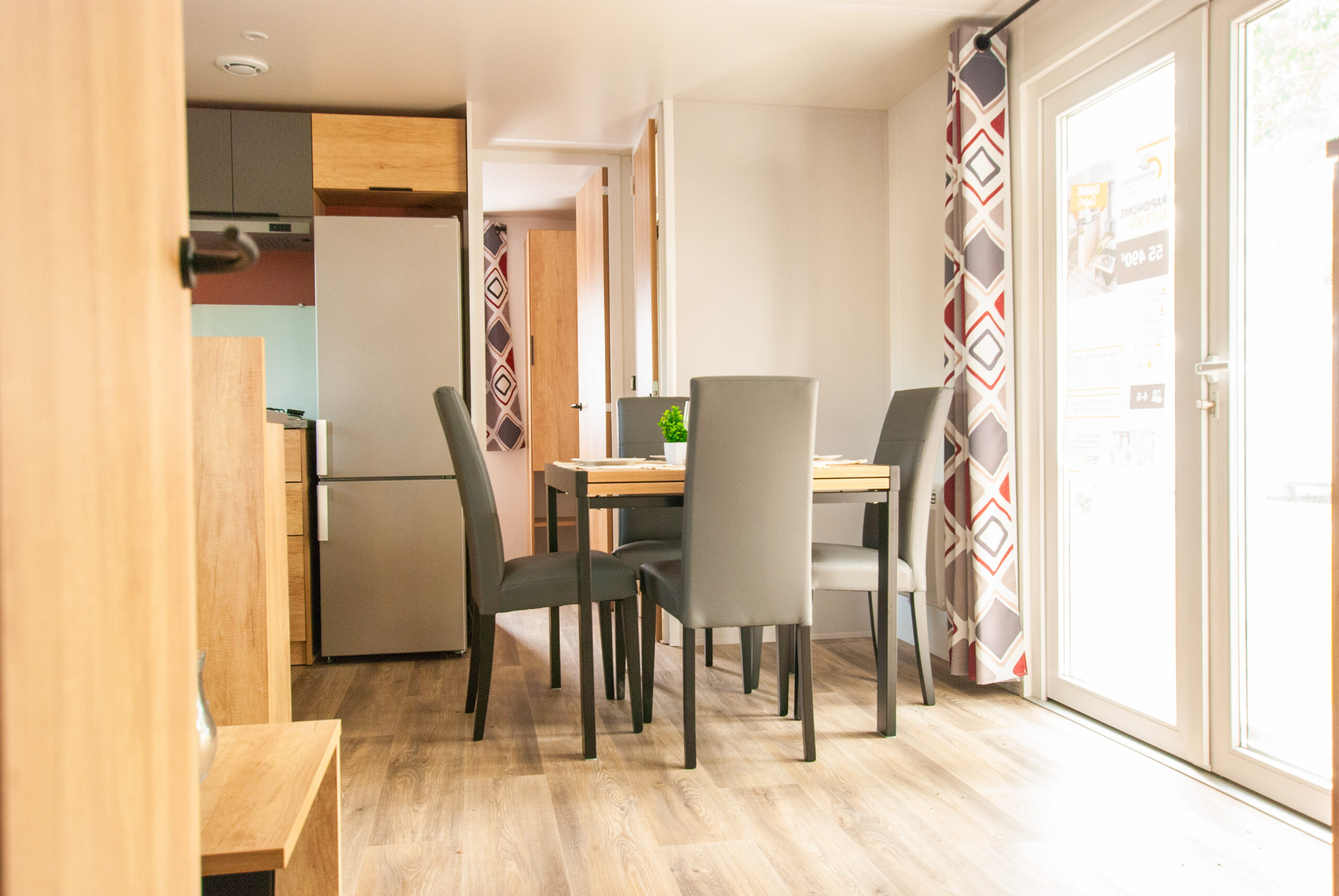 Luminoso interior de una casa móvil Rapid'home Elite 902 en venta en las Landas, mostrando la mesa del salón ideal para comidas para 4 personas, rodeada de grandes ventanales y un mirador.