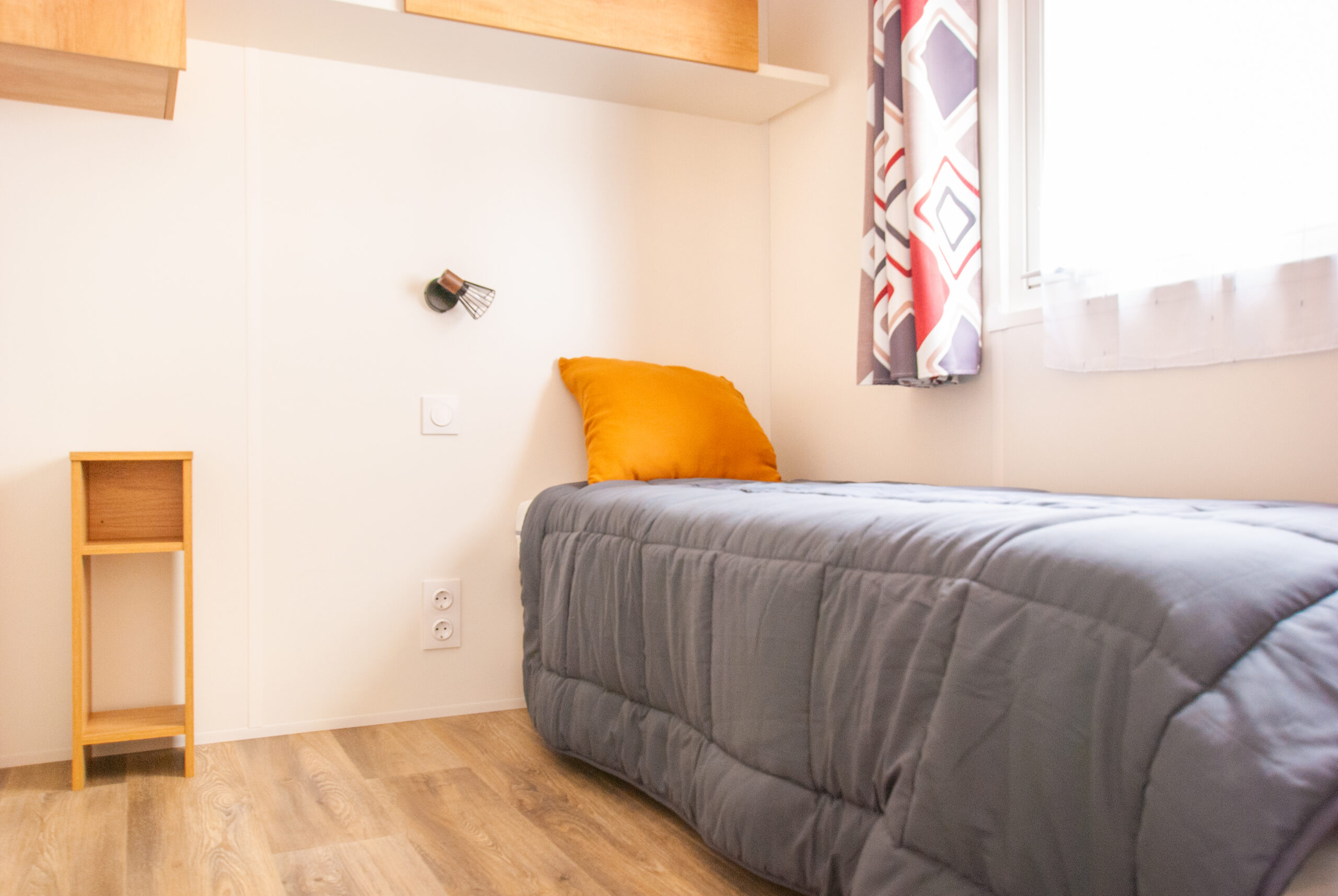Intérieur d'un mobil home Rapid'home Élite 1040 avec première chambre lumineuse, lit simple et fenêtre, idéal pour vos vacances dans les Landes, 2 salles de bains et 3 chambres.