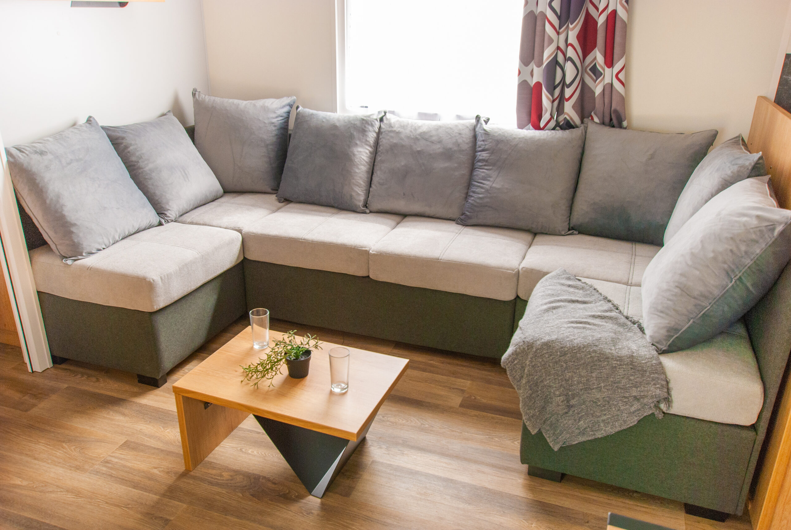 Intérieur du mobil-home Rapid'home Élite 1040 avec vue sur le canapé confortable et la fenêtre lumineuse, offrant une ambiance spacieuse et accueillante, avec 2 salles de bains et 3 chambres, à vendre dans les Landes.