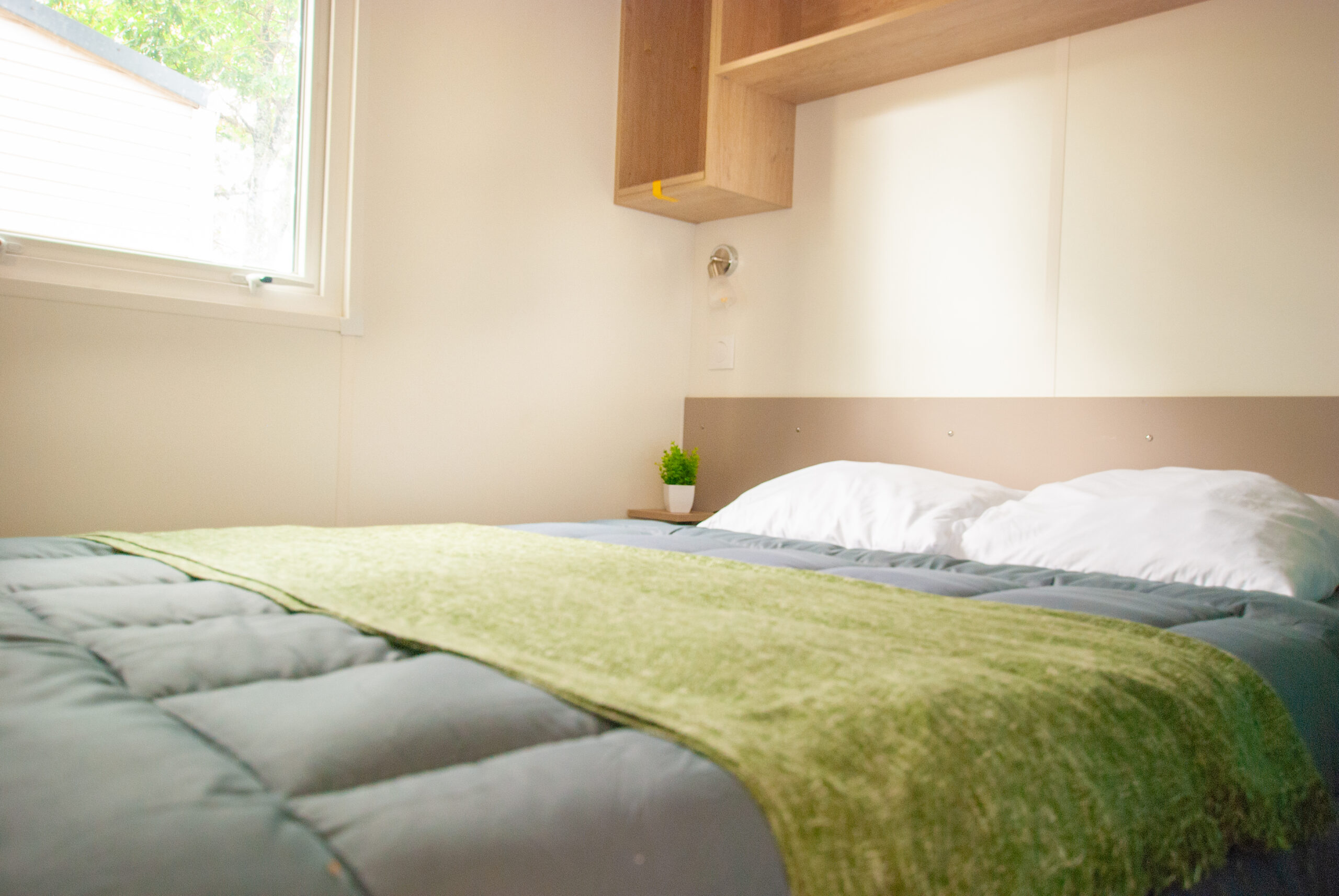 Intérieur du mobil home Rapid'home lodge 83 - Chambre parentale avec grand lit deux places, bien éclairée par une fenêtre, offrant confort idéal pour couples et familles dans les Landes