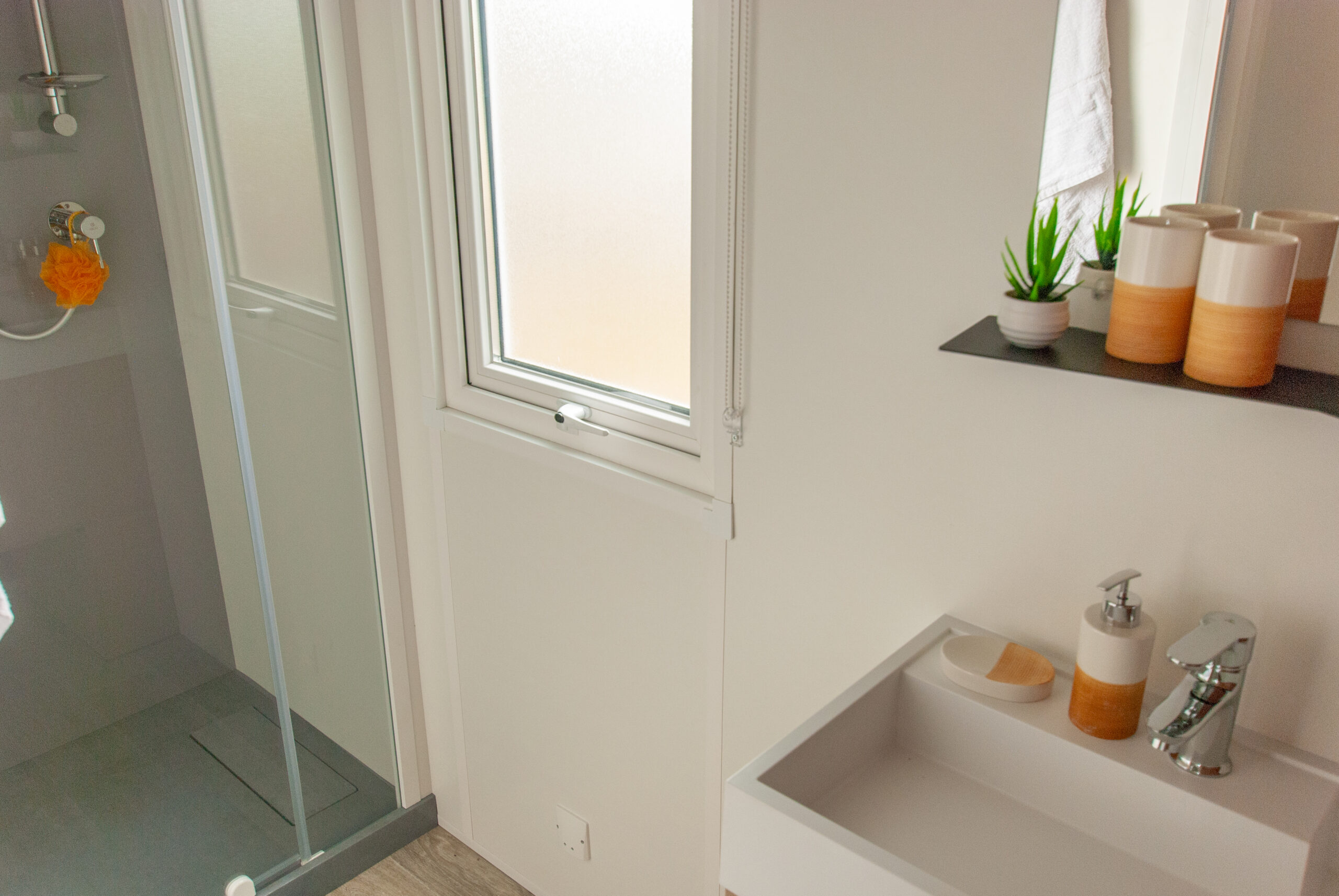 Intérieur mobil home Rapid'home LO872 à vendre dans les Landes - salle de bains moderne avec douche, lavabo, miroir et fenêtre, alliant praticité et confort.