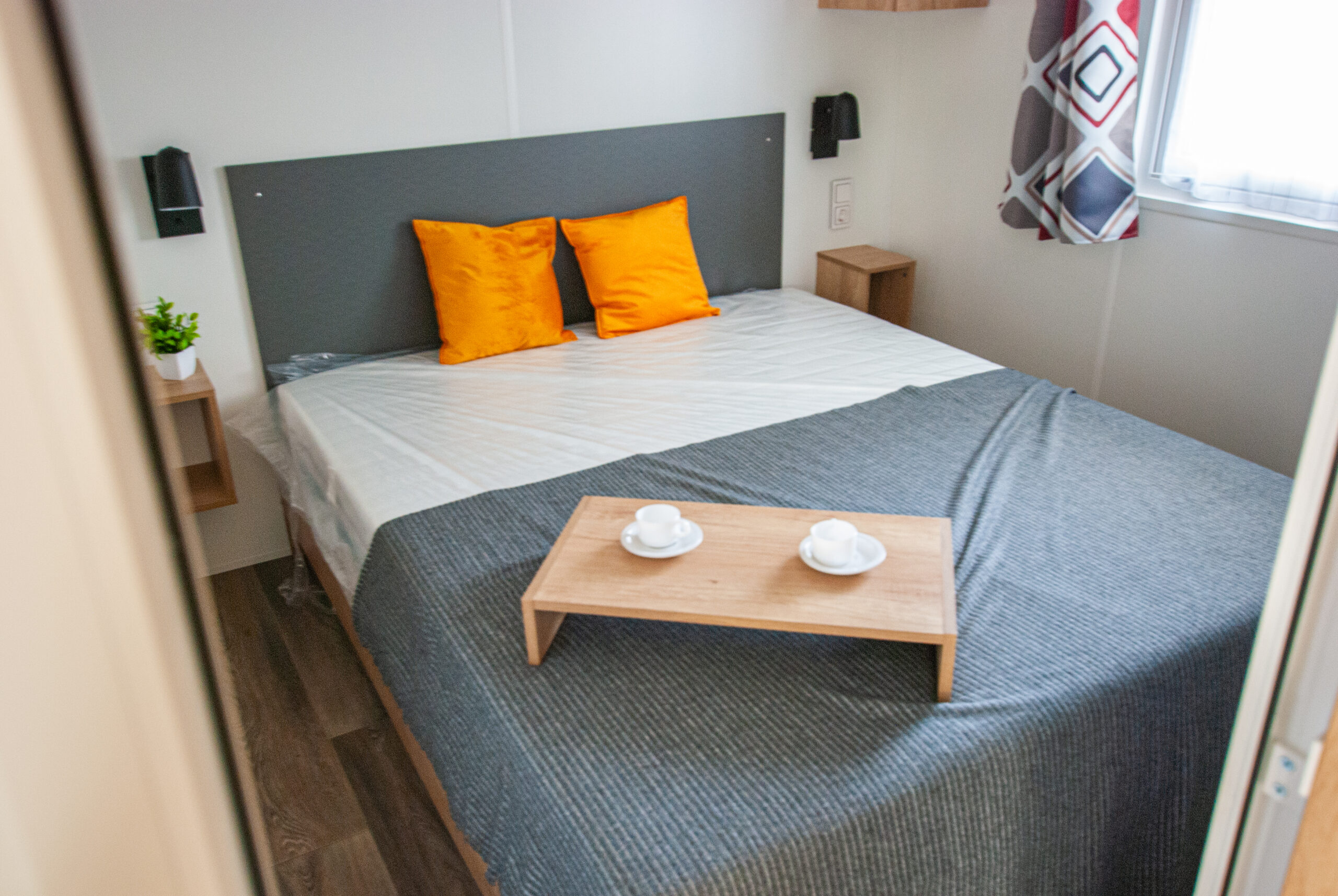 Dormitorio principal en el Rapid'home Elite 902 casa móvil en venta en las Landas con cama doble y bandeja de desayuno en la cama